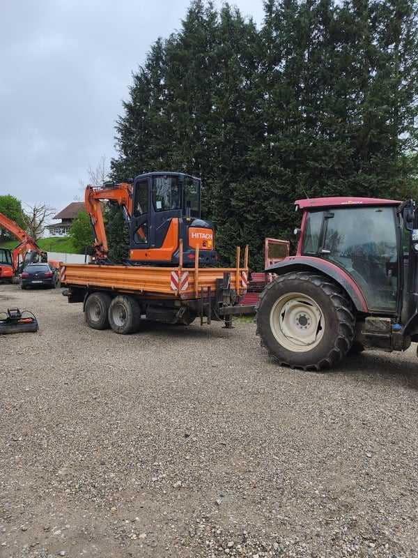 Auf Anhänger verladener Minibagger, gezogen von einem Traktor